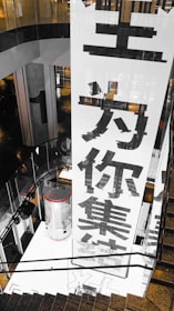 A large vertical banner with bold Chinese characters is displayed, dominating the interior space of a modern building. The architecture features dark reflective surfaces and a combination of industrial and sleek design elements.
