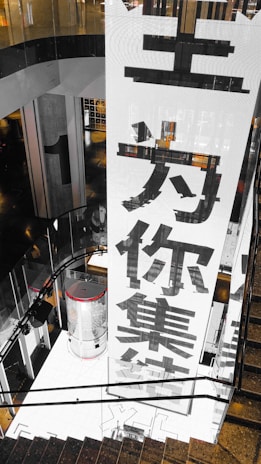 A large vertical banner with bold Chinese characters is displayed, dominating the interior space of a modern building. The architecture features dark reflective surfaces and a combination of industrial and sleek design elements.