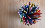 Close-up of a rubber band stretched around colorful pencils on a desk