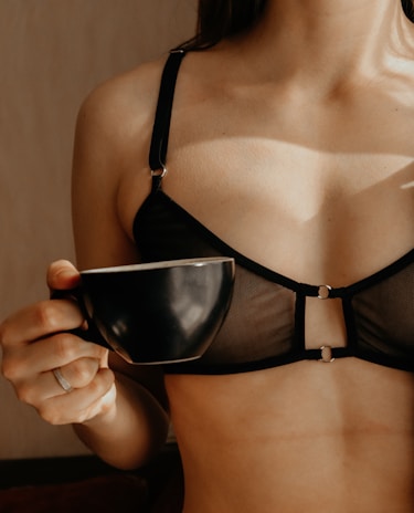 A person wearing a black mesh bra is holding a black coffee cup.