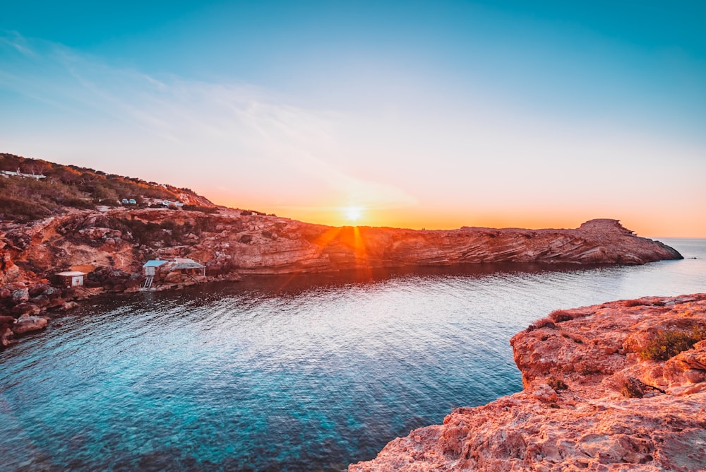 Montaña rocosa marrón al lado del cuerpo de agua durante la puesta del sol