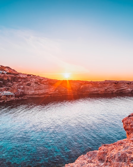 brown rocky mountain beside body of water during sunset