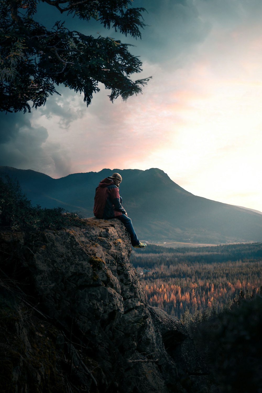 woman in brown jacket sitting on rock near green grass field and mountain during daytime