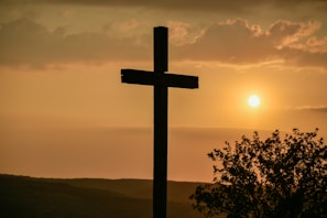 A close-up of a rustic cross against a sunset backdrop.