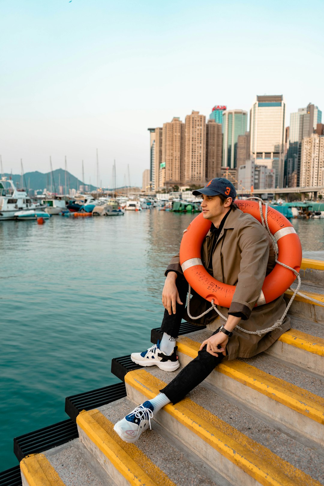 man in orange t-shirt and brown pants sitting on concrete dock during daytime