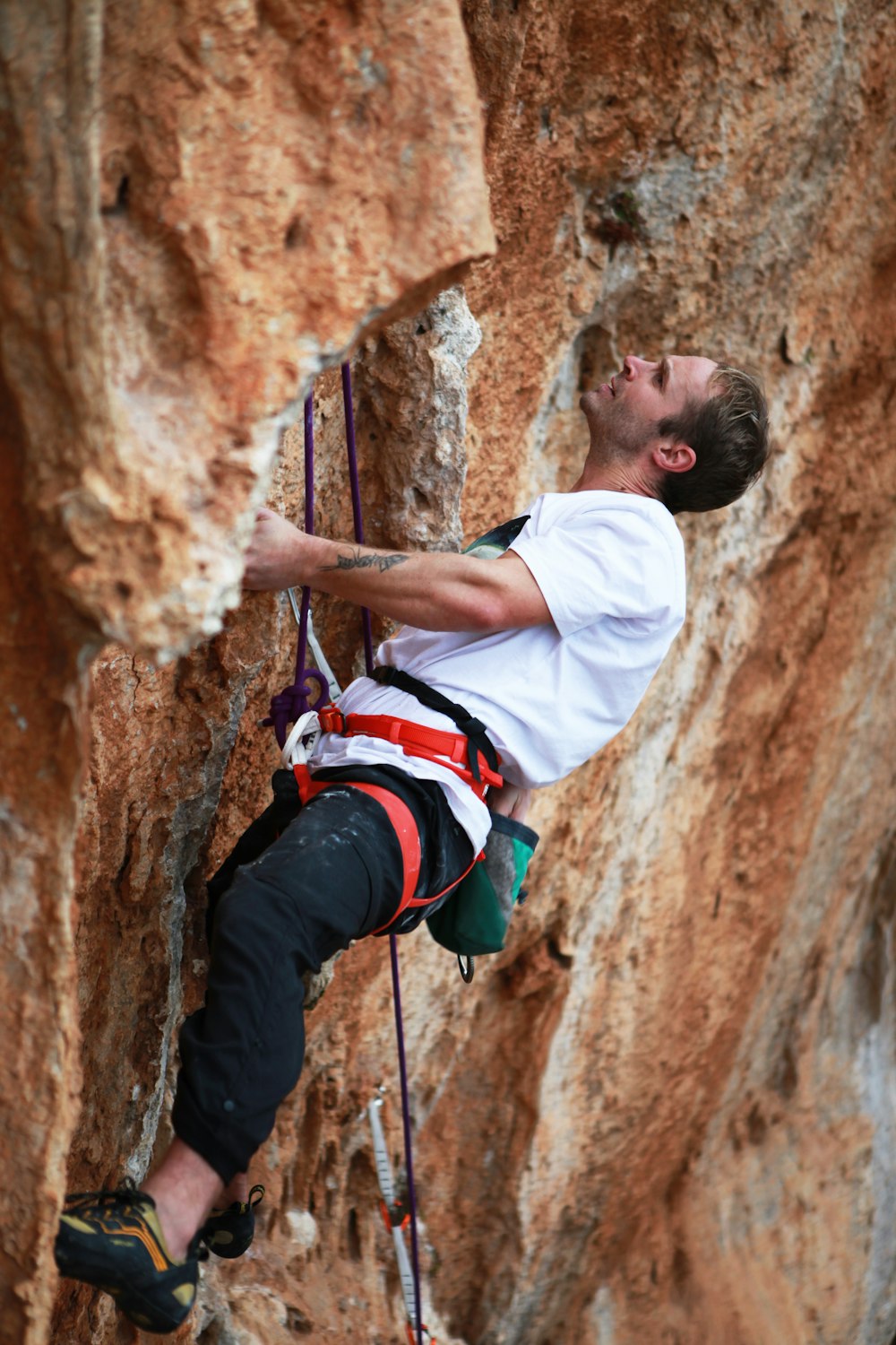 man in white shirt climbing on brown rock