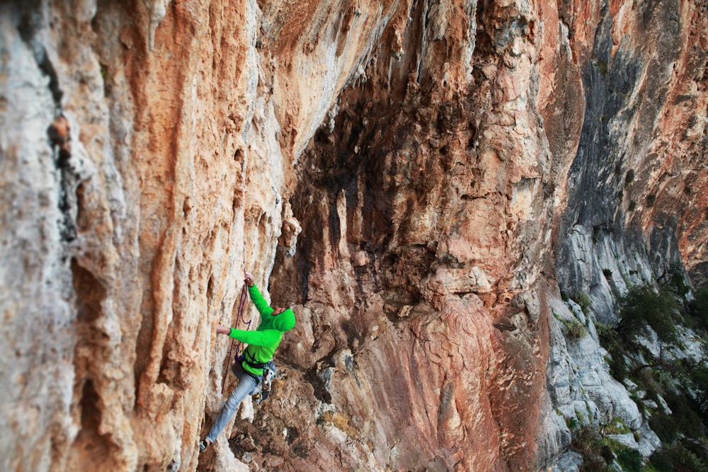 man in green jacket climbing on brown rock
