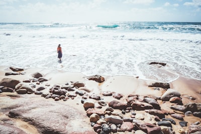 woman in white shirt and blue denim shorts standing on beach shore during daytime