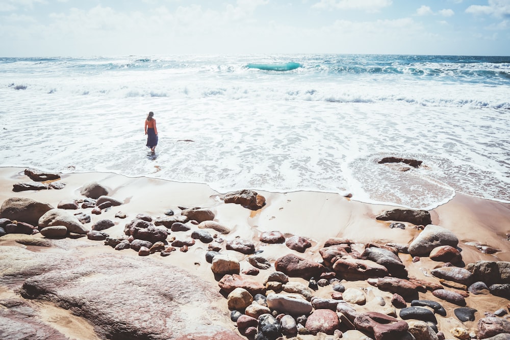 woman in white shirt and blue denim shorts standing on beach shore during daytime