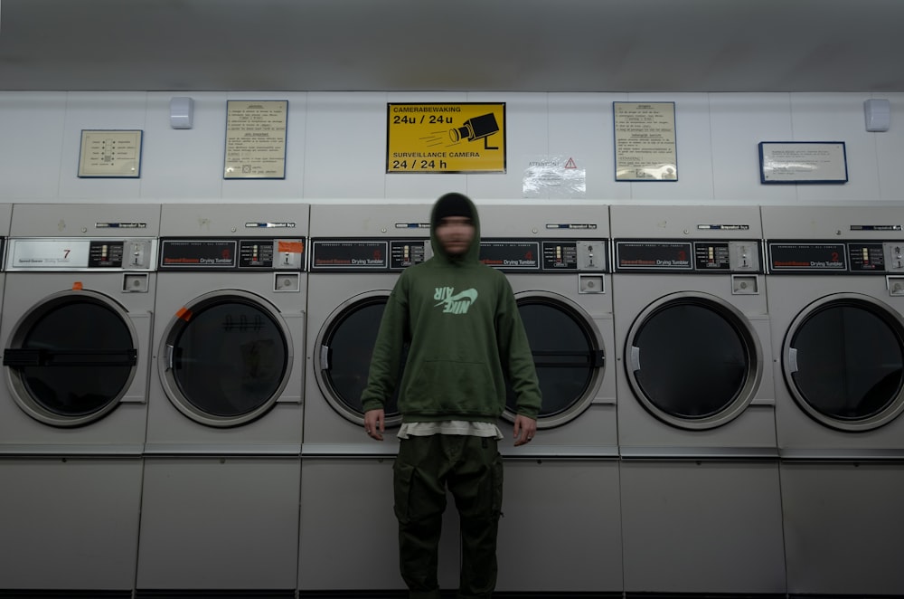 man in green hoodie standing beside front load washing machine