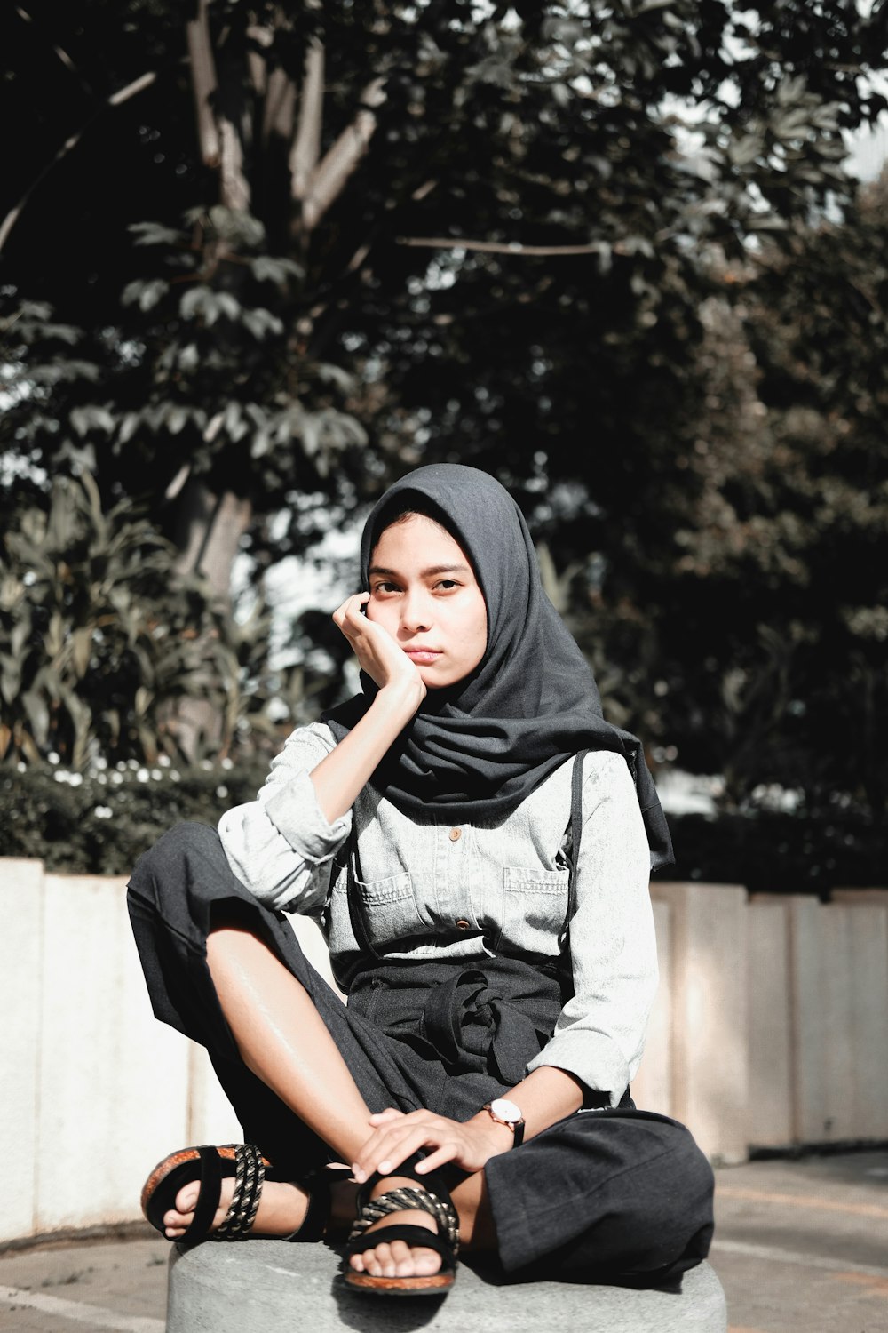 검은 히잡과 회색 긴팔 셔츠를 입고 콘크리트 벤치에 앉아 있는 여자