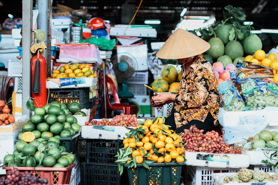 woman in brown and white floral dress standing in front of fruit stand,