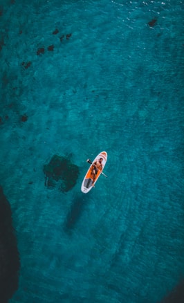person riding on white and red surfboard on body of water during daytime