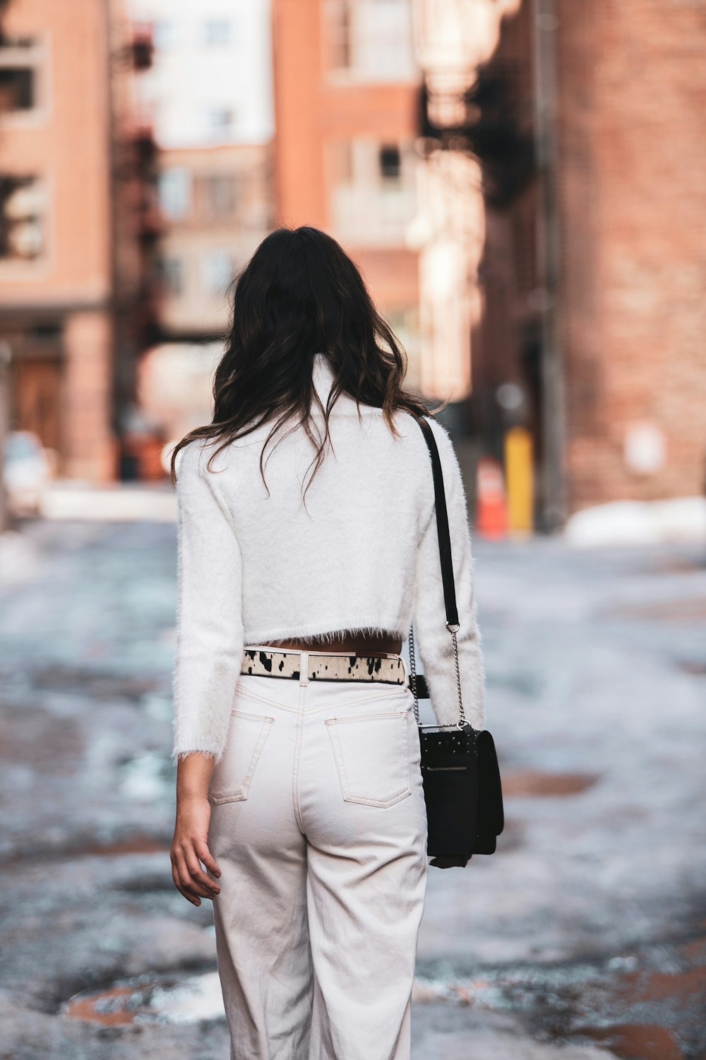 woman in white long sleeve shirt and gray pants walking on street during daytime