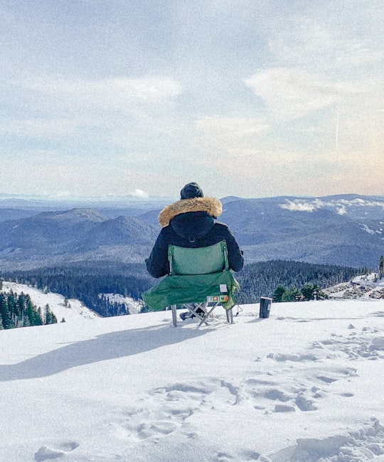 man in green jacket sitting on green chair on snow covered ground during daytime in Timberline Lodge and Ski Area United States