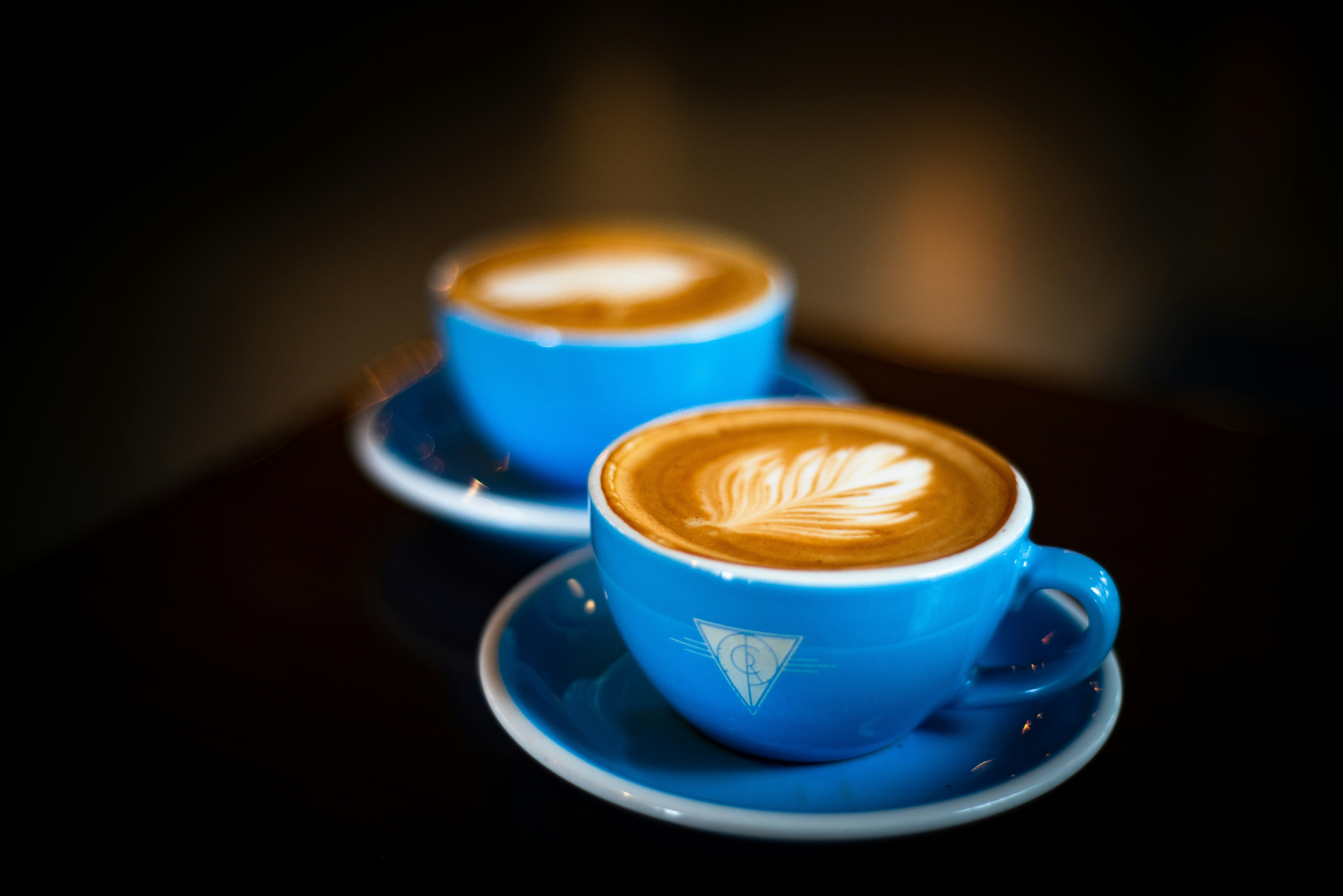 Two lattes in blue cups on a dark table