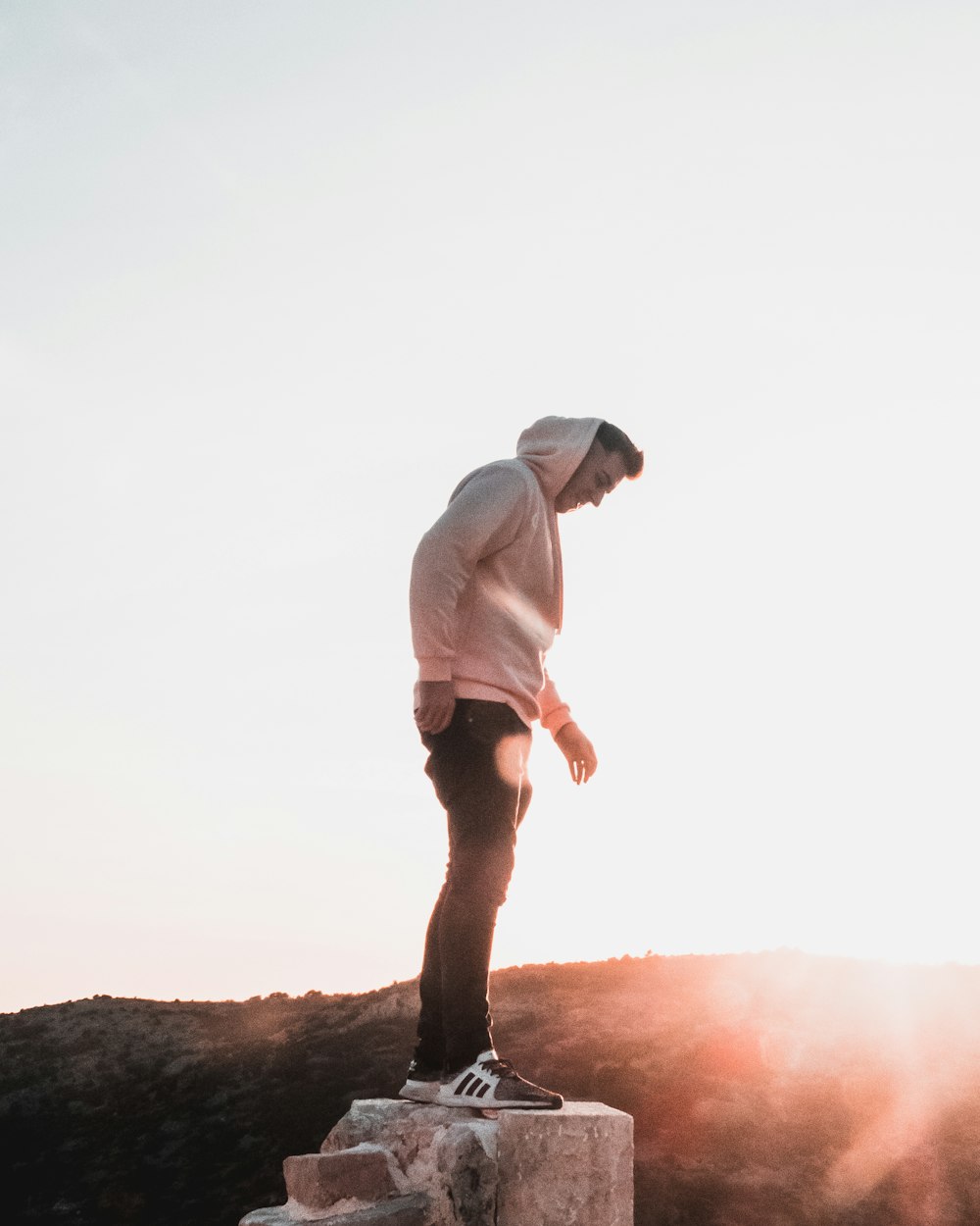 man in gray hoodie and black shorts standing on brown rock during daytime