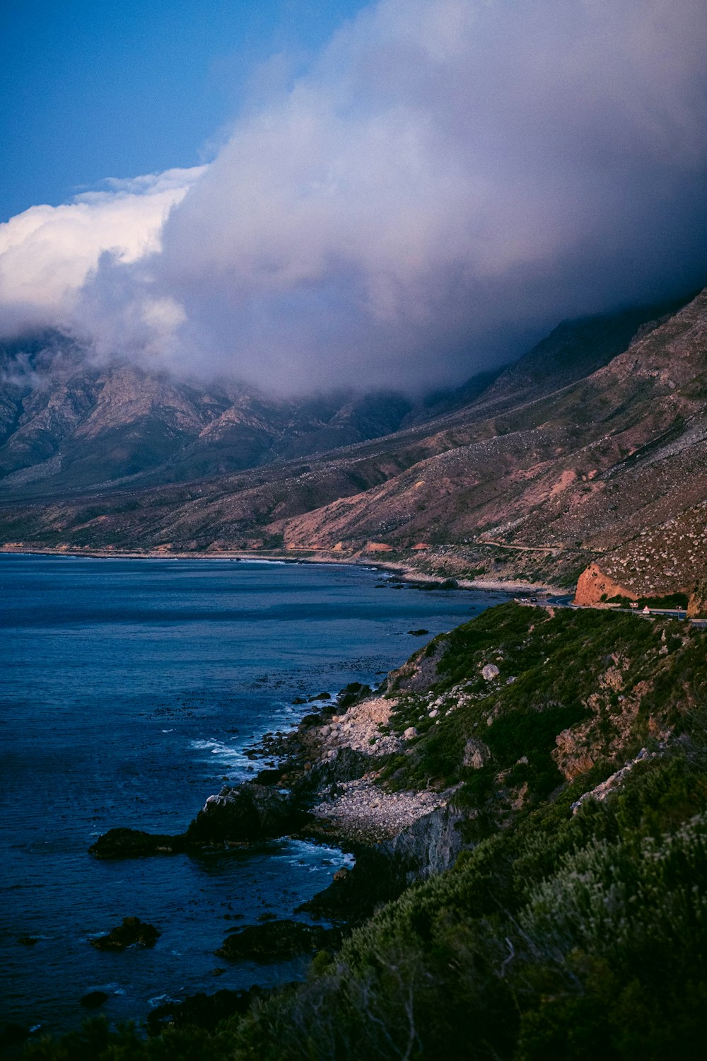 montagne brune et verte au bord de la mer bleue sous les nuages blancs pendant la journée