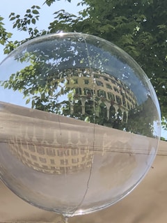 A transparent bubble reflects a building with multiple windows and surrounding green foliage. The scene captures the essence of a serene outdoor setting on a clear day.