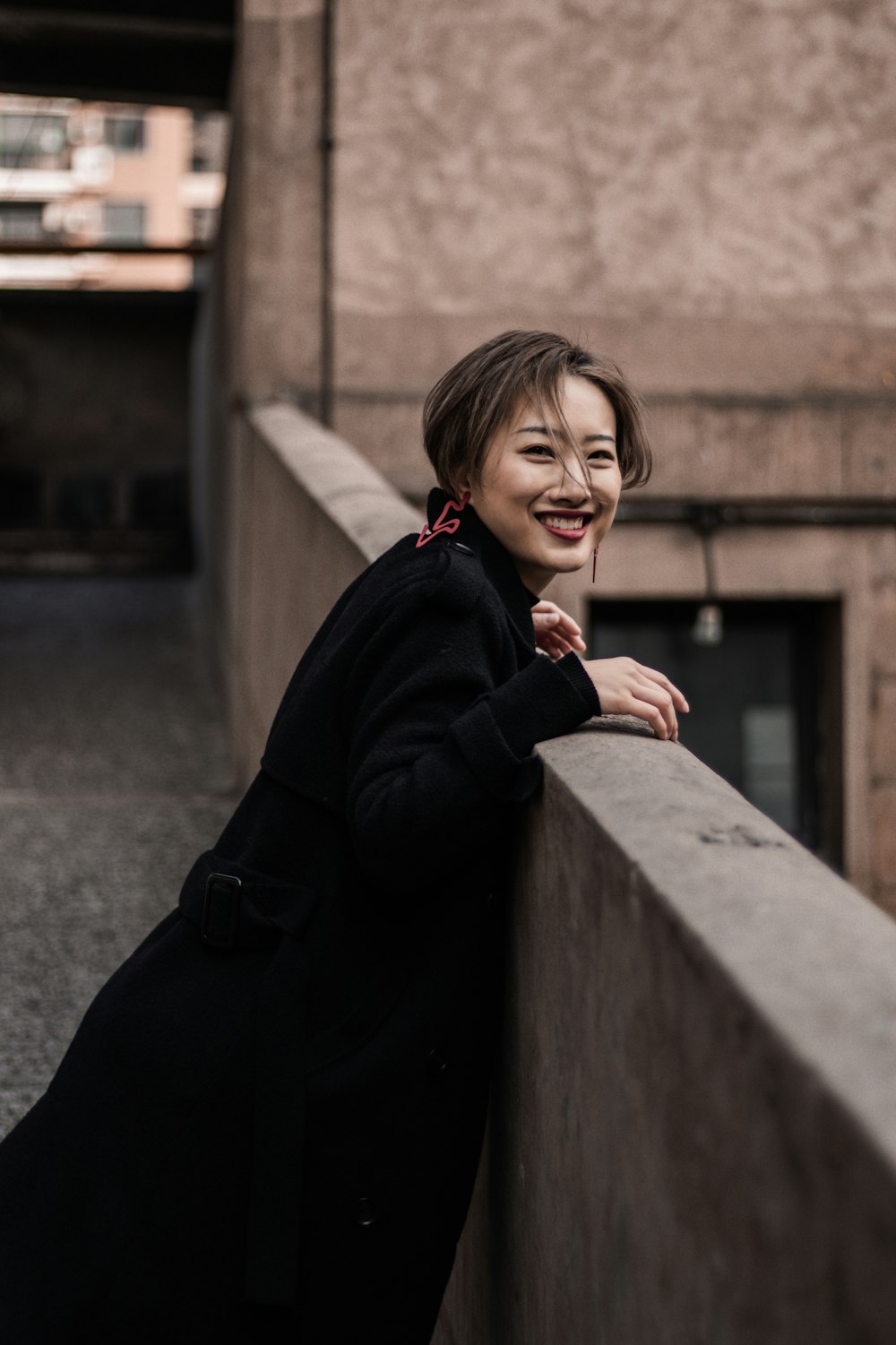 woman in black jacket leaning on concrete wall during daytime