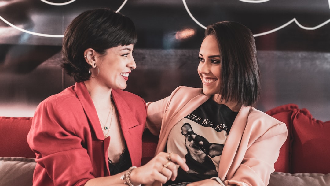 woman in red blazer beside woman in black and white floral dress