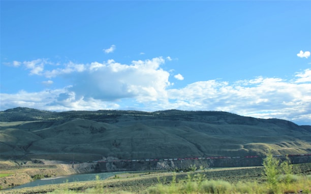 A scenic view of a small train crossing a green valley under a bright blue sky.