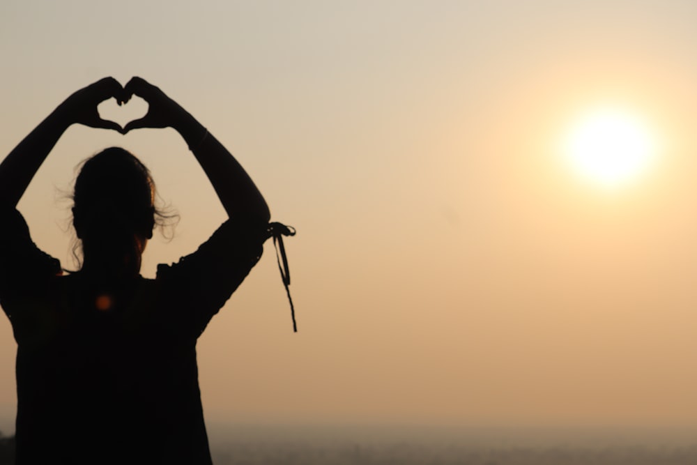 silhouette of woman raising her hands during sunset