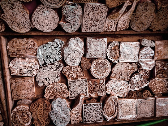 Intricately carved wooden blocks with various patterns and designs, including animals and geometric shapes, are arranged in a wooden drawer.
