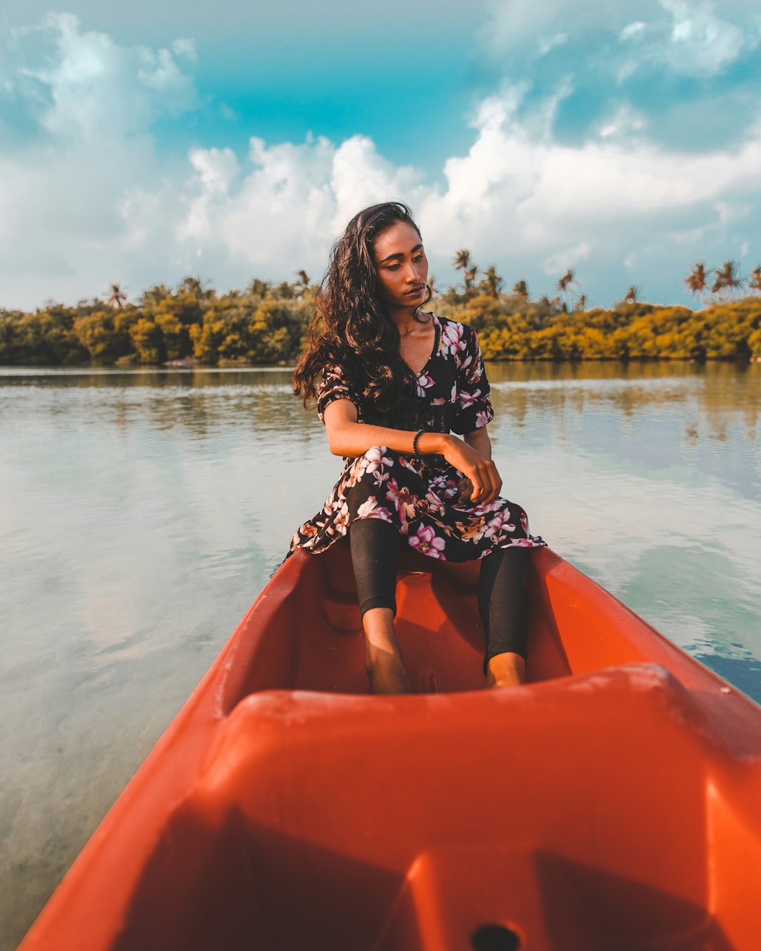 woman in black and white floral long sleeve shirt sitting on orange kayak on lake during