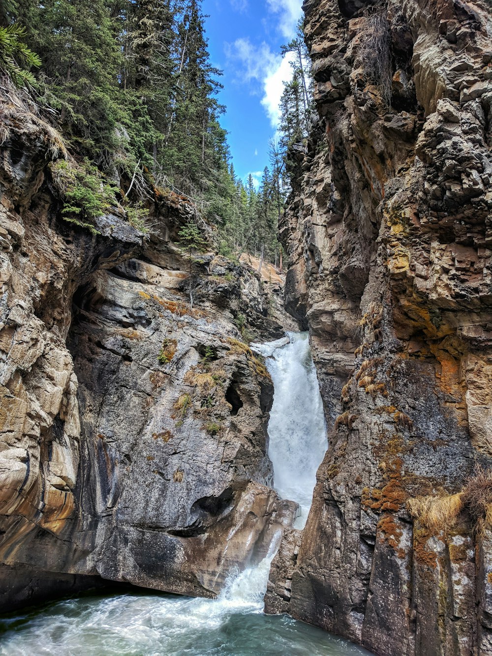 waterfalls between brown rocky mountain under blue sky during daytime