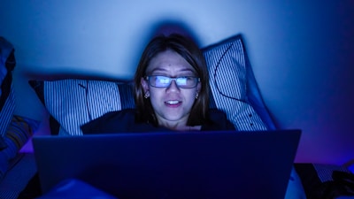 Close-up of a person reading a digital guide on a laptop in a dimly lit room with deep blue lighting.