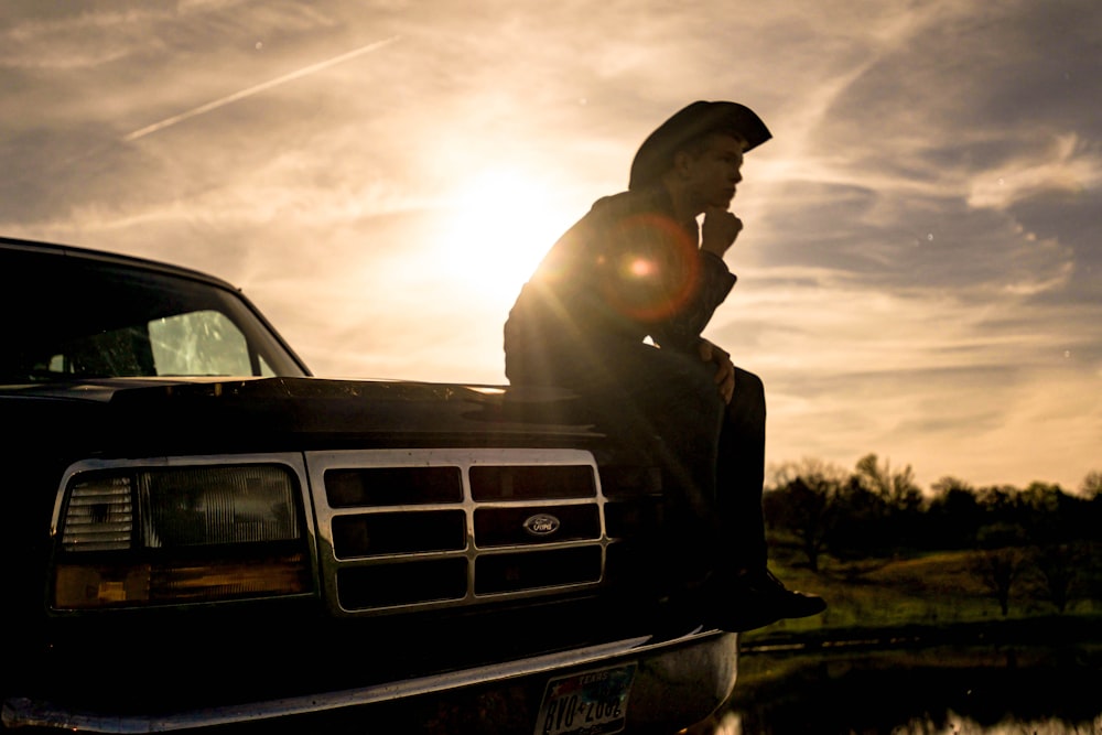 man in black jacket and black cap sitting on black car hood during daytime