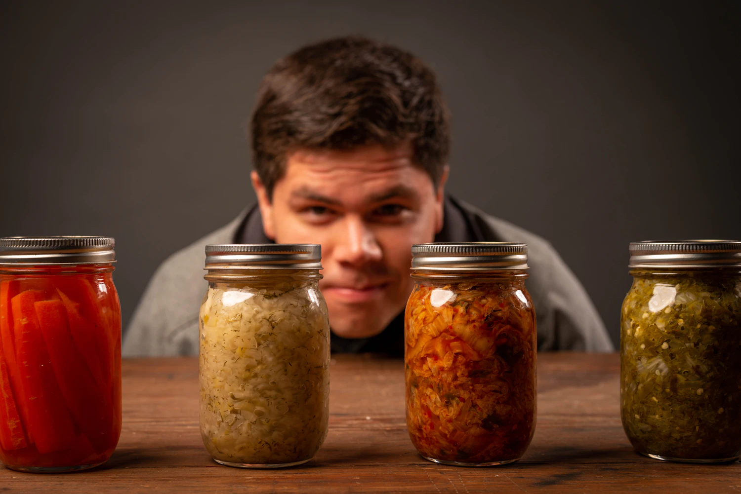 Four jars of preserves standing in a row on a dark wooden table