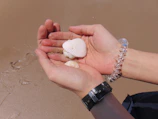 Delicate sea shells resting on soft sand beside a woven bracelet with natural fibers.