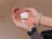 Two hands gently hold seashells with grains of sand visible, against a backdrop of sandy ground. A clear, plastic bracelet is worn on one wrist, adding a touch of modernity.