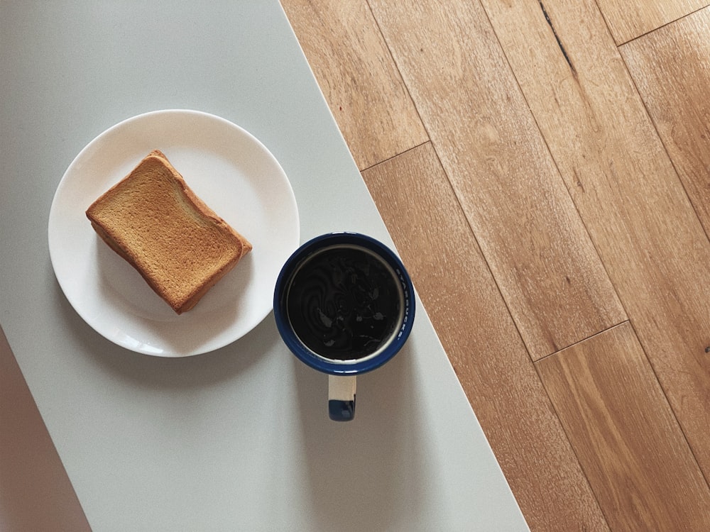 a piece of toast on a plate next to a cup of coffee