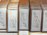 A collection of chocolate bars arranged neatly in rows, with vintage-style packaging featuring intricate blue designs and cursive script on a white background. The bars are labeled 'Vollmilch Extra Fein' indicating fine milk chocolate.