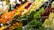 A vibrant and colorful market display showcasing a variety of fresh fruits and vegetables, including red, green, and yellow peppers, eggplants, oranges, and cabbages. The produce is stacked neatly in baskets and crates, creating an appealing and inviting scene.