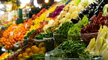 A vibrant and colorful market display showcasing a variety of fresh fruits and vegetables, including red, green, and yellow peppers, eggplants, oranges, and cabbages. The produce is stacked neatly in baskets and crates, creating an appealing and inviting scene.