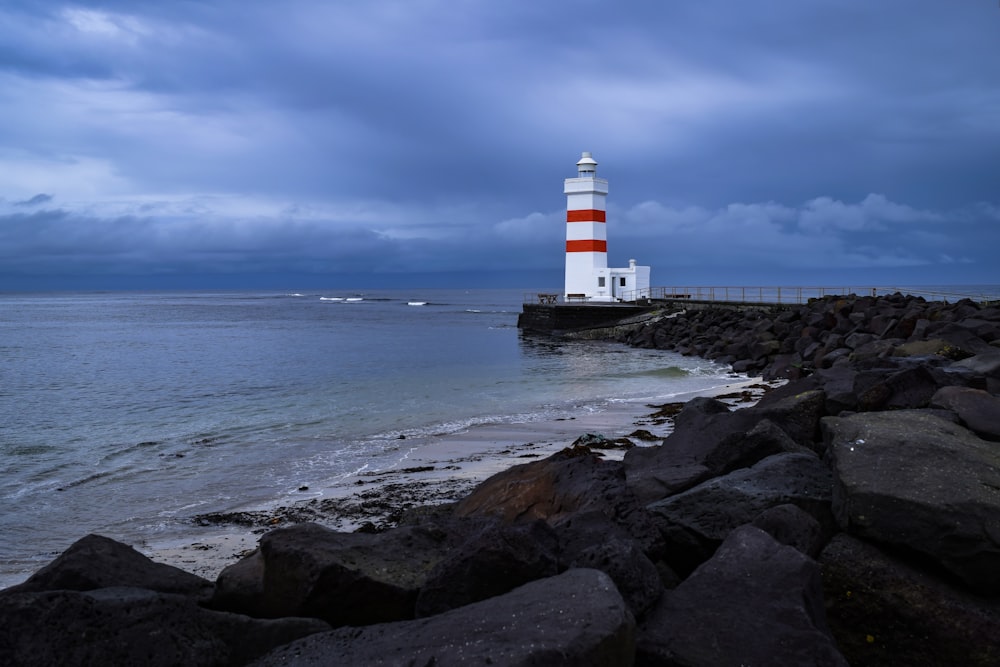 farol branco e vermelho na costa rochosa marrom durante o dia