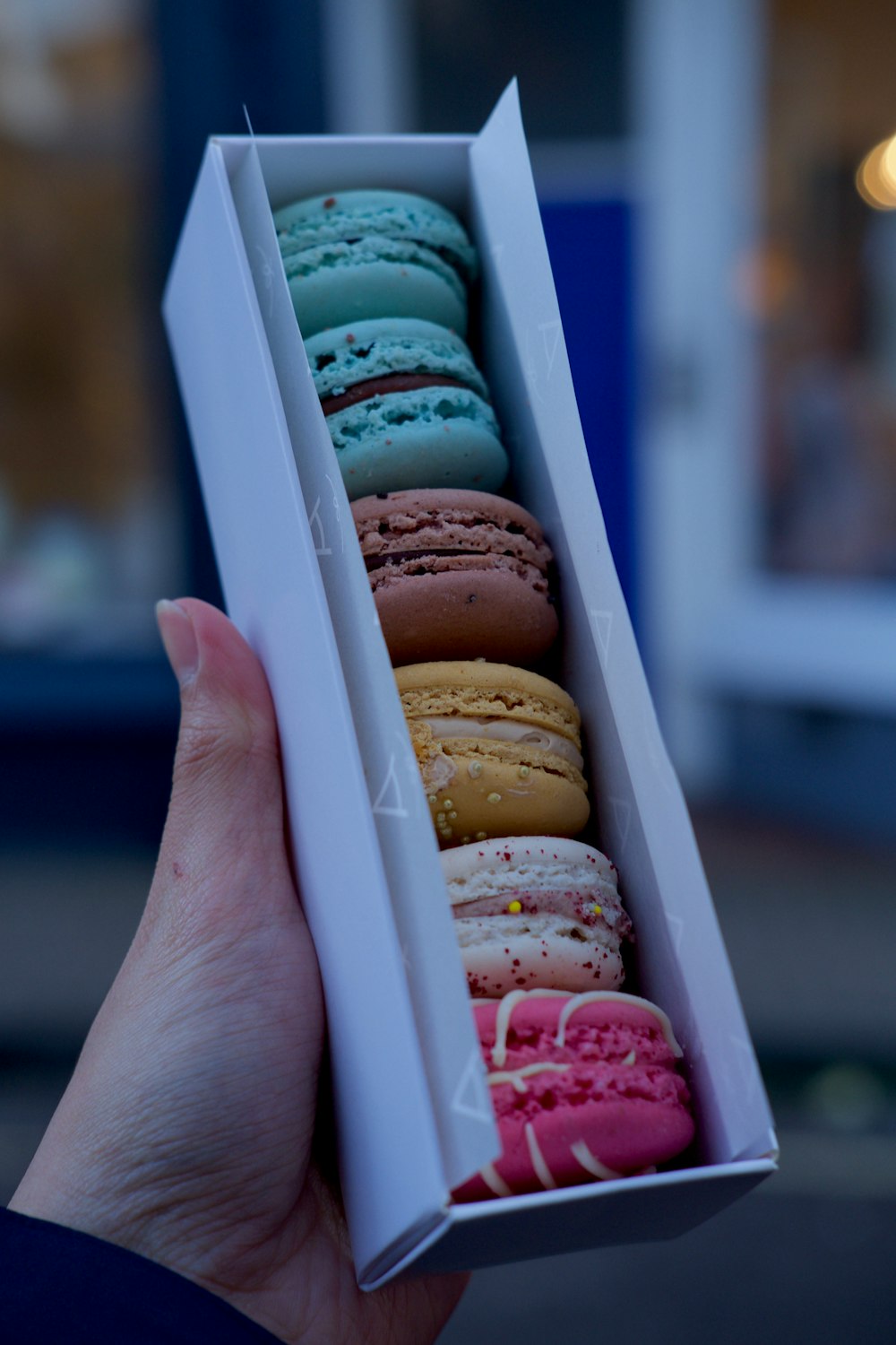 person holding 3 brown and white donuts in white box