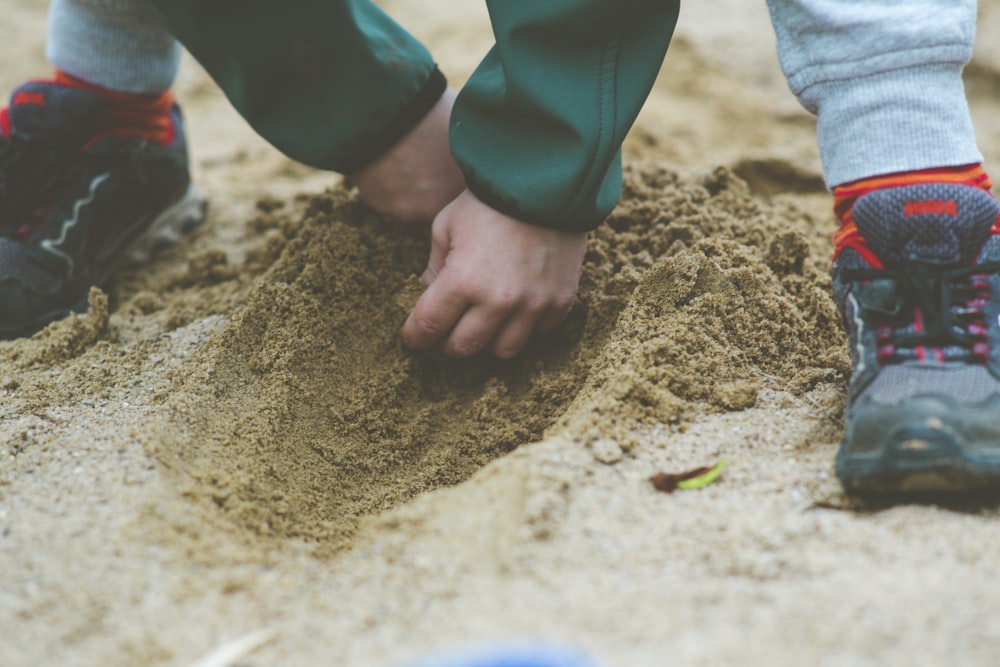 person in blue long sleeve shirt and blue denim jeans standing on brown sand during daytime