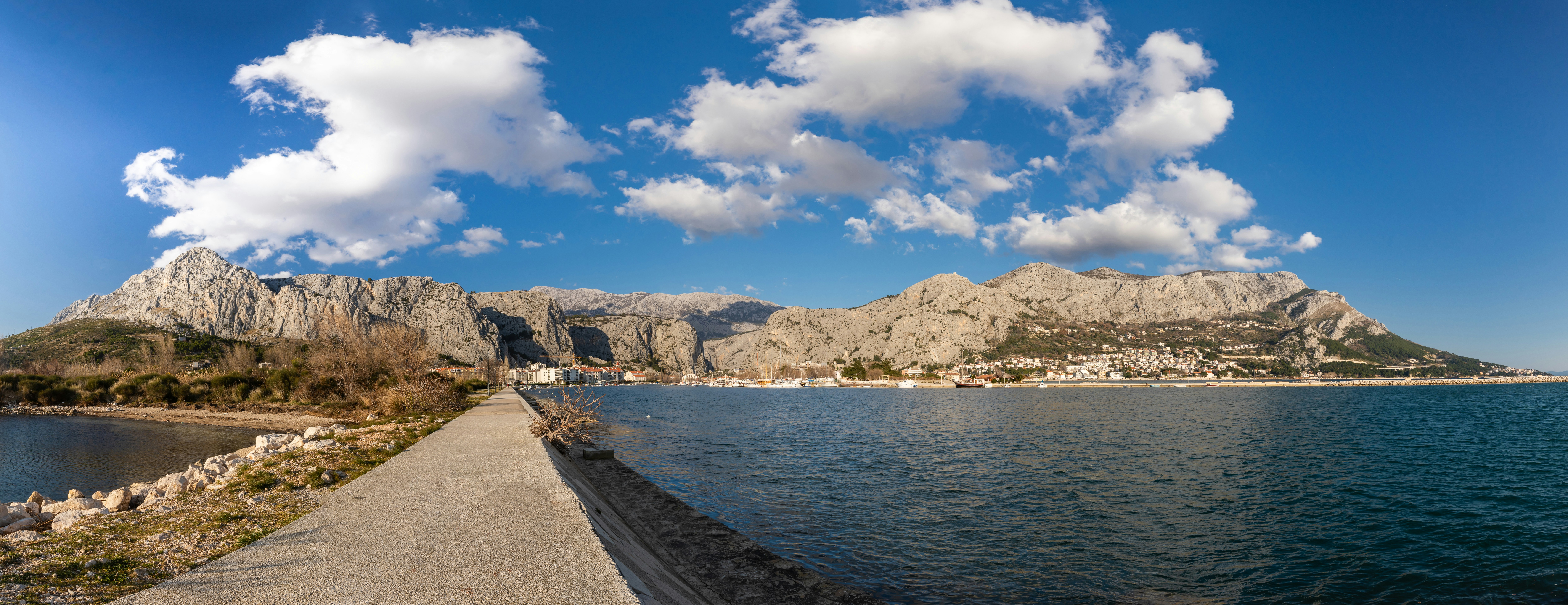 brown wooden dock on sea near brown mountain under blue sky and white clouds during daytime