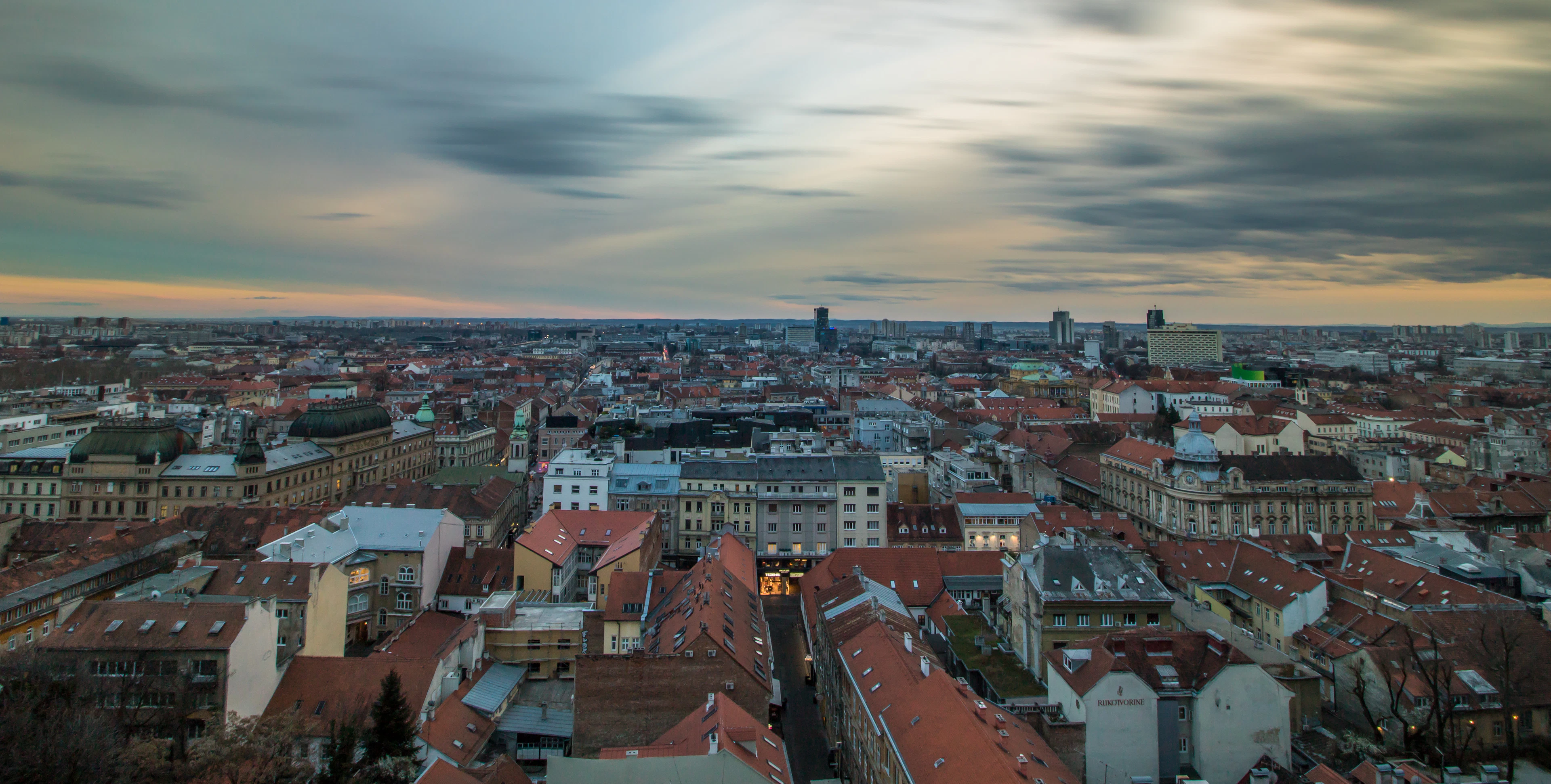 Aerial view across the red-tiled rooftops of central Zagreb at dusk, with the city's modern towers on the horizon, Croatia