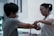 Two individuals are engaged in an activity where one person is tying the wrists of the other with a rope. Both are focused, and the setting appears to be indoors with soft lighting.
