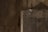 A close-up view of a weathered concrete wall with a rough, textured surface. The wall shows signs of aging with cracks and darker patches, suggesting exposure to the elements over time. The lighting casts shadows that enhance the texture and detail of the concrete.