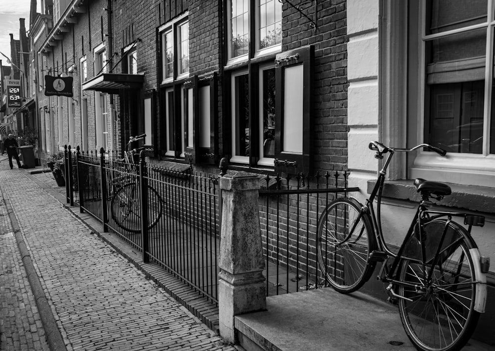 grayscale photo of bicycle parked beside building