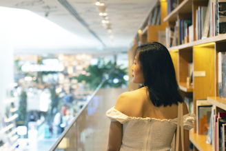 woman in white off shoulder dress standing near glass wall
