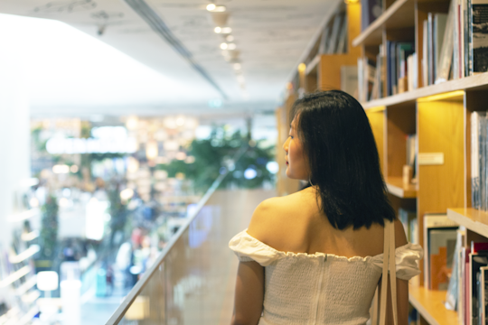 woman in white off shoulder dress standing near glass wall
