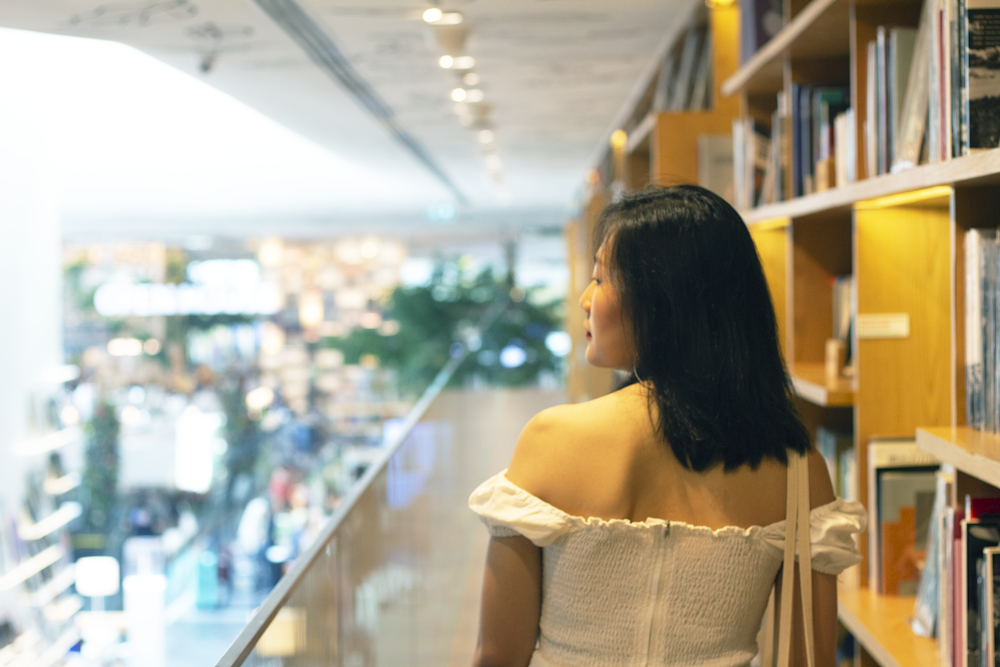 woman in white off shoulder dress standing near glass wall